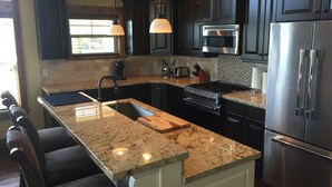 Una cocina moderna con encimeras de granito, electrodomésticos de acero inoxidable y muebles oscuros.
