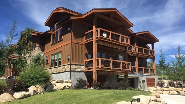 Una casa de madera de varios pisos con balcones, ventanas amplias y un cimiento de piedra.