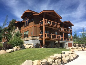 A multi-story wooden house with balconies, large windows, and a stone foundation.