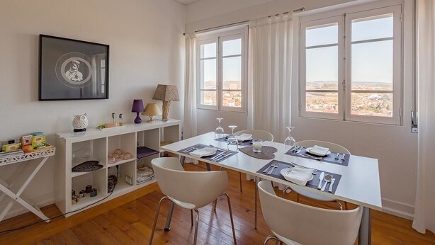 A dining area with a white table set for two, a white chair, and a shelf with various items. - Casa da Real Companhia (Lamego)