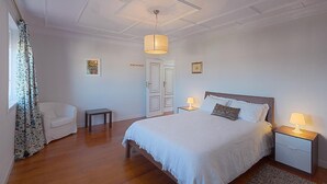 A bedroom with a large bed, bedside tables with lamps, a chair, a small table, and a door. - Casa da Real Companhia (Lamego)