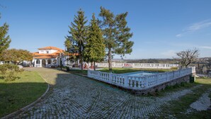 A cobblestone pathway leading to a white building with a red-tiled roof, surrounded by trees and a white fence. - Casa da Real Companhia (Lamego)