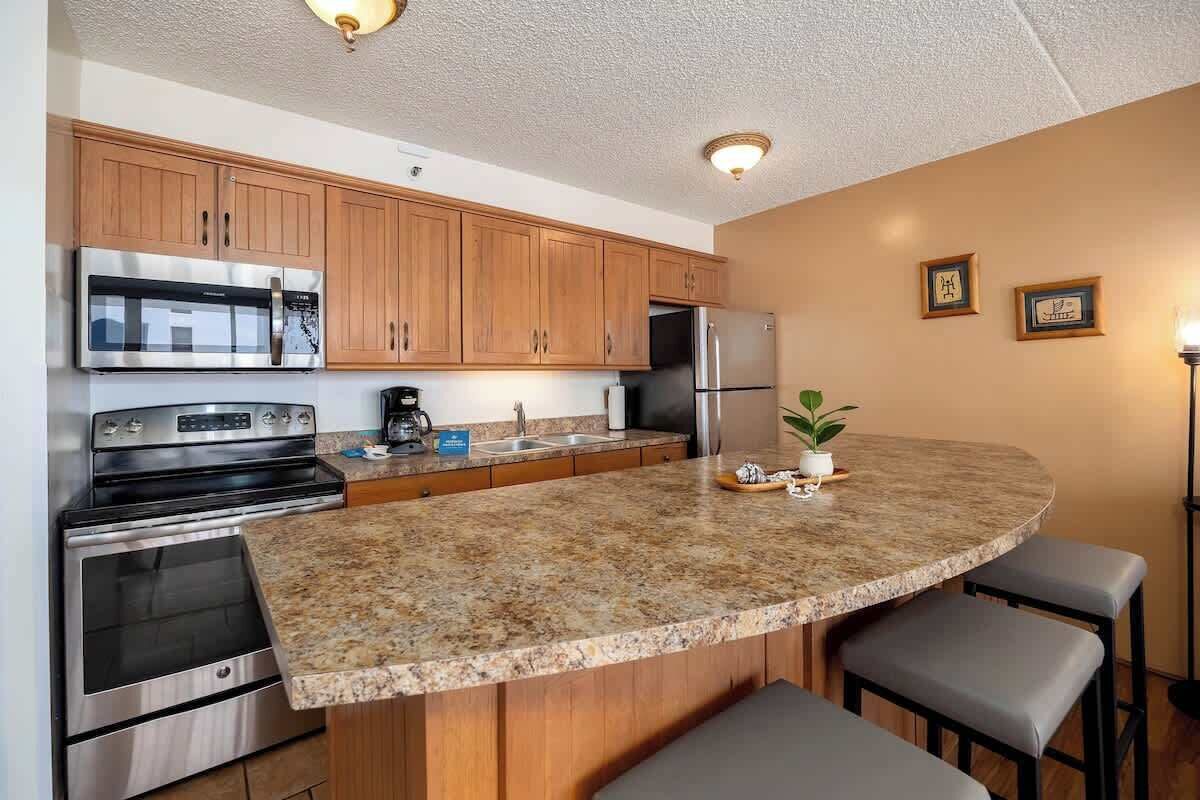 A kitchen with wooden cabinets, stainless steel appliances, a granite countertop, and a bar stool.