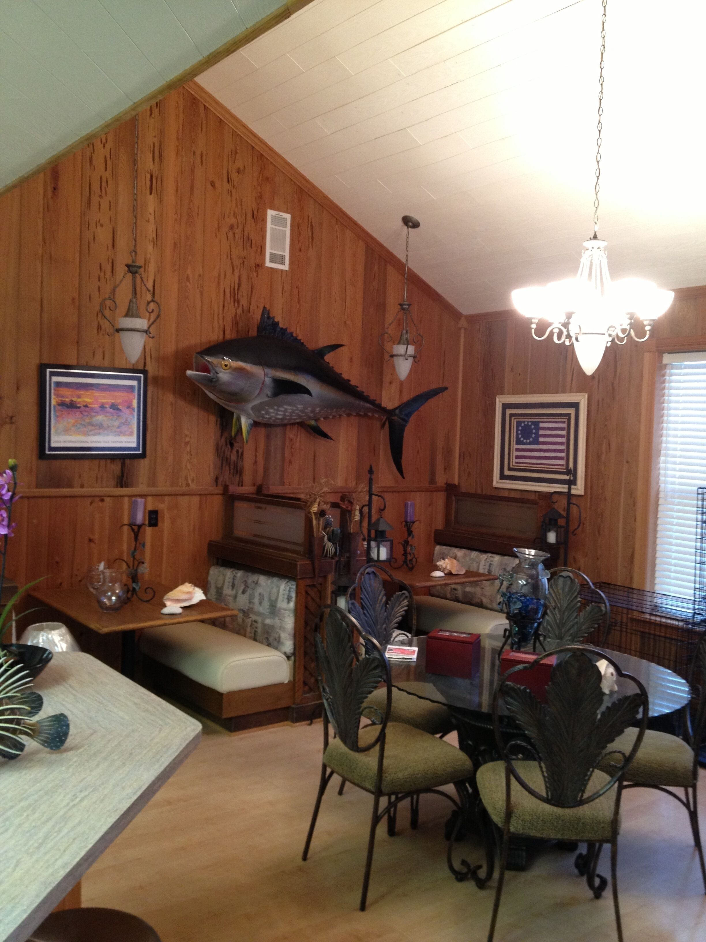 A wooden interior with a dining table, chairs, a chandelier, and a large fish mounted on the wall.