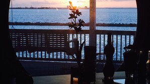 Vista de uma área externa coberta, com corrimão, para um corpo de água e um pôr do sol.