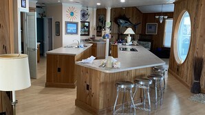 Uma cozinha ampla com painéis de madeira, uma ilha grande com banquetas, uma janela redonda e um ventilador de teto.