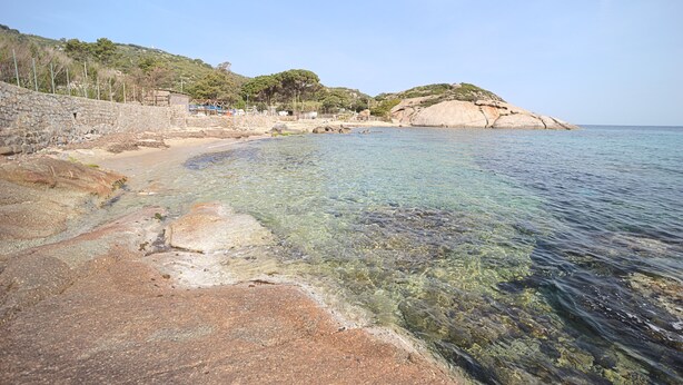 A coastal beach with clear waters, rocky shore, and a small building on the left. - CASA MARGOT (RELAX WITH VISTA), independent, 300mt from the sea and the beach (Isola del Giglio)