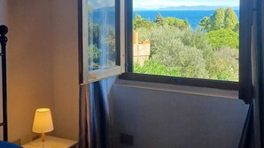 A bedroom with a bed, a nightstand, a lamp, and a window with a view of the sea and greenery. - CASA MARGOT (RELAX WITH VISTA), independent, 300mt from the sea and the beach (Isola del Giglio)