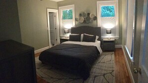 Une chambre à coucher avec un grand lit, deux tables de chevet avec des lampes, un canapé de couleur foncée et un tapis à motifs.
