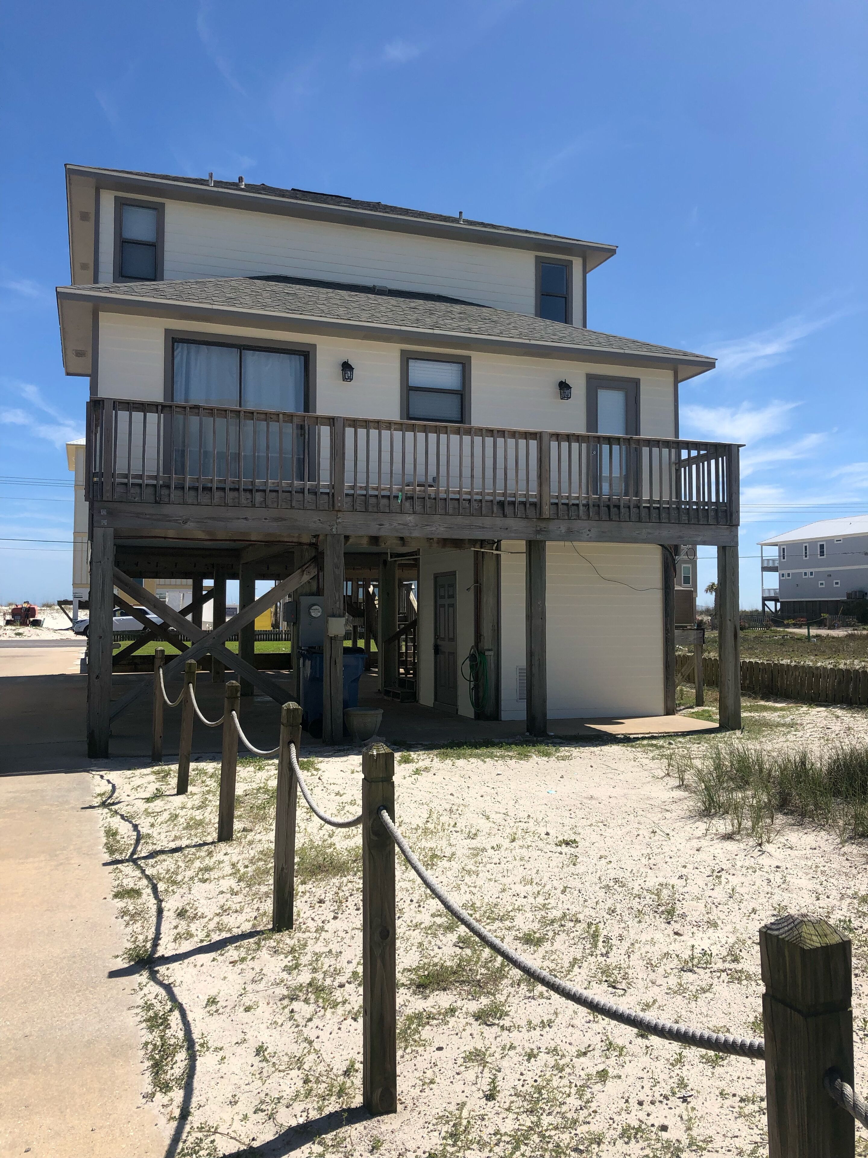 A two-story building with a balcony, a covered entrance, and a sandy ground area with a wooden fence.