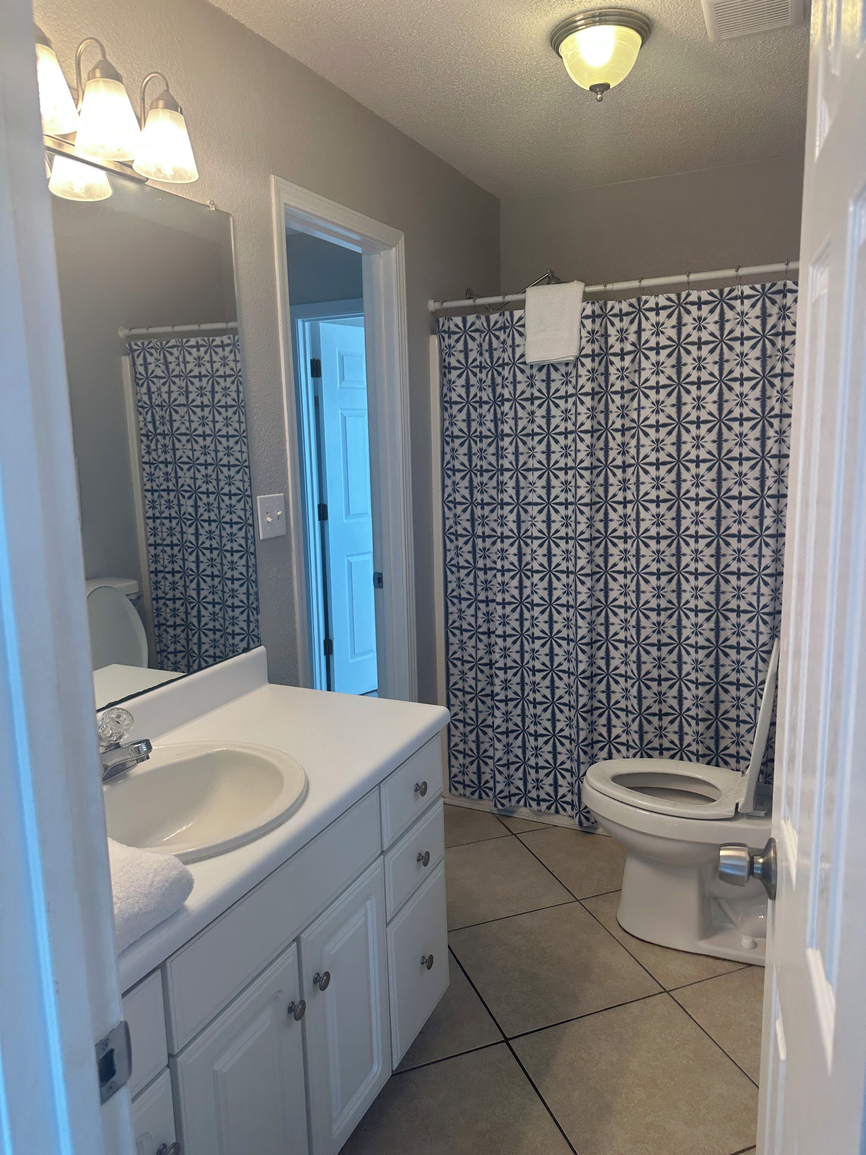 A bathroom with a white sink, mirror, and toilet. There is a patterned shower curtain and a towel hanging on the wall.