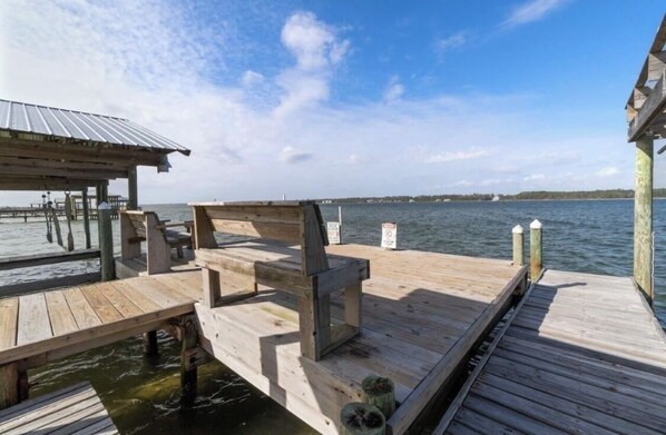 A wooden dock extending into a body of water with a covered seating area and a view of the water and distant shoreline.