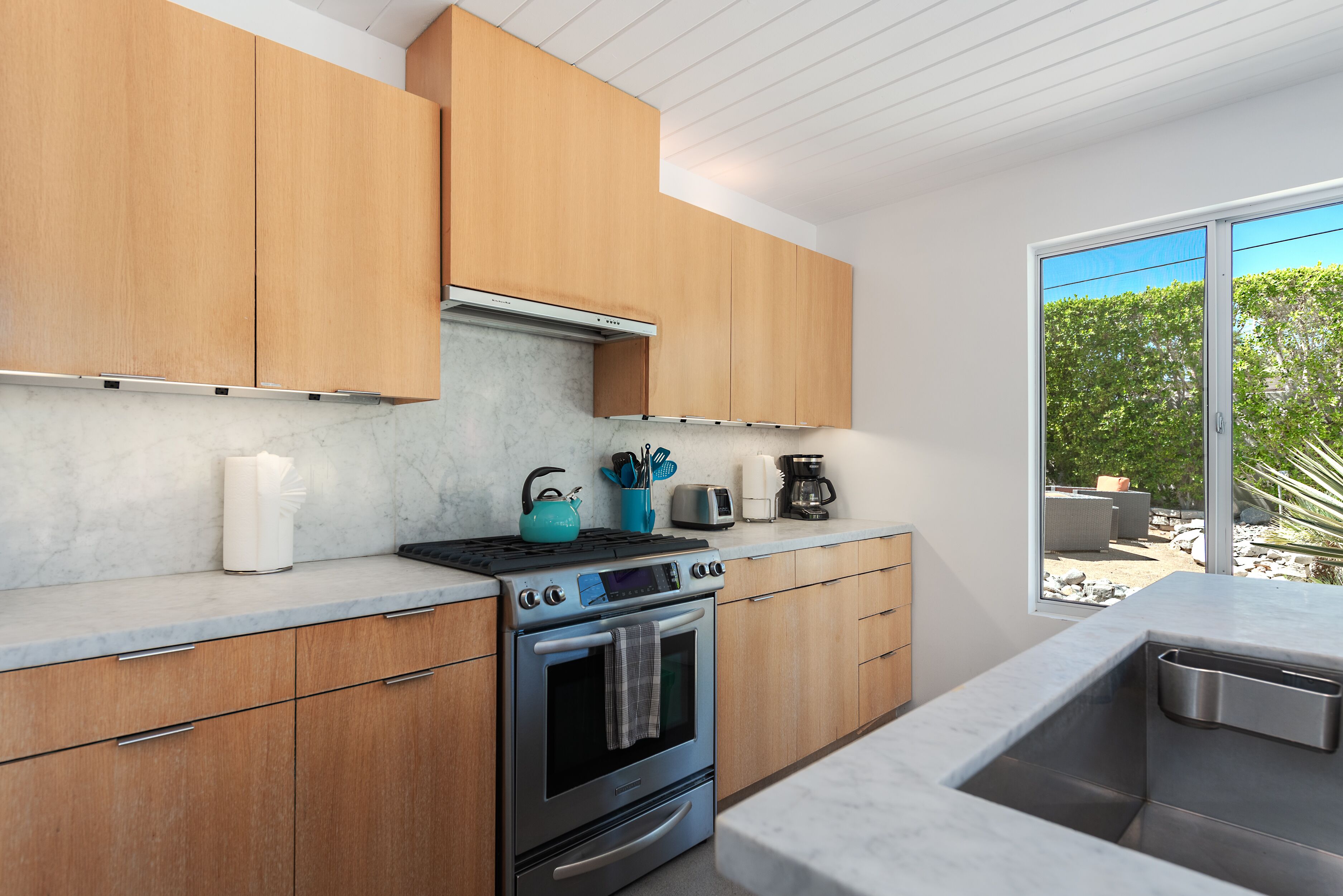 A modern kitchen with wooden cabinets, a stainless steel oven, and a large window offering a view of the outdoors.