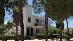 A two-story building with a balcony, surrounded by trees and a gravel courtyard. - La Palude del Conte (Porto Cesareo)