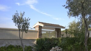 A covered outdoor area with a pergola, surrounded by various plants and a stone wall. - La Palude del Conte (Porto Cesareo)