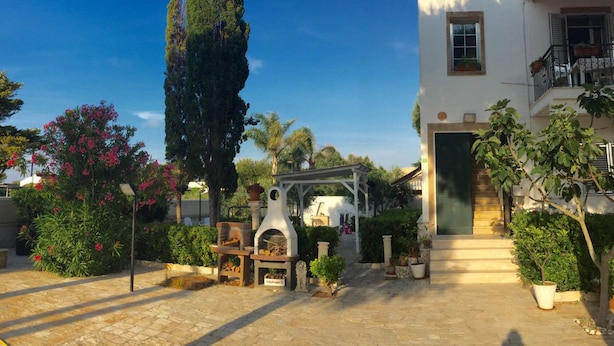 A courtyard with a stone pathway, a pergola, a small outdoor grill, and potted plants. - La Palude del Conte (Porto Cesareo)