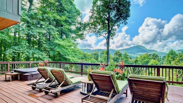 A wooden deck with lounge chairs and a small table, overlooking a lush green landscape with trees and a mountain in the distance. - Highlands Happy Place (Highlands)