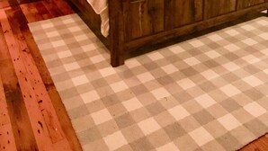 A bedroom with a wooden bed, checkered rug, and white walls. - Highlands Happy Place (Highlands)