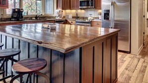 A spacious kitchen with wooden cabinets, a large island with stools, stainless steel appliances, and a window providing natural light. - Highlands Happy Place (Highlands)