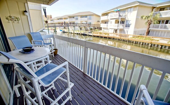 Ein Balkon mit weißen Stühlen und einem Tisch, der auf einen Yachthafen mit Booten und einem Gebäude mit Balkonen blickt.