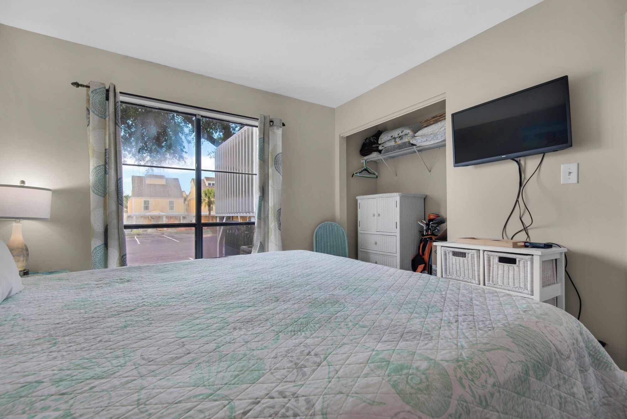 A bedroom with a large bed, a television mounted on the wall, a wardrobe, and a window with curtains.