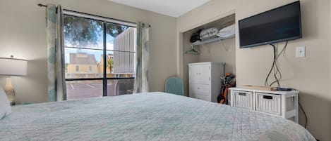 A bedroom with a large bed, a television mounted on the wall, a wardrobe, and a window with curtains.