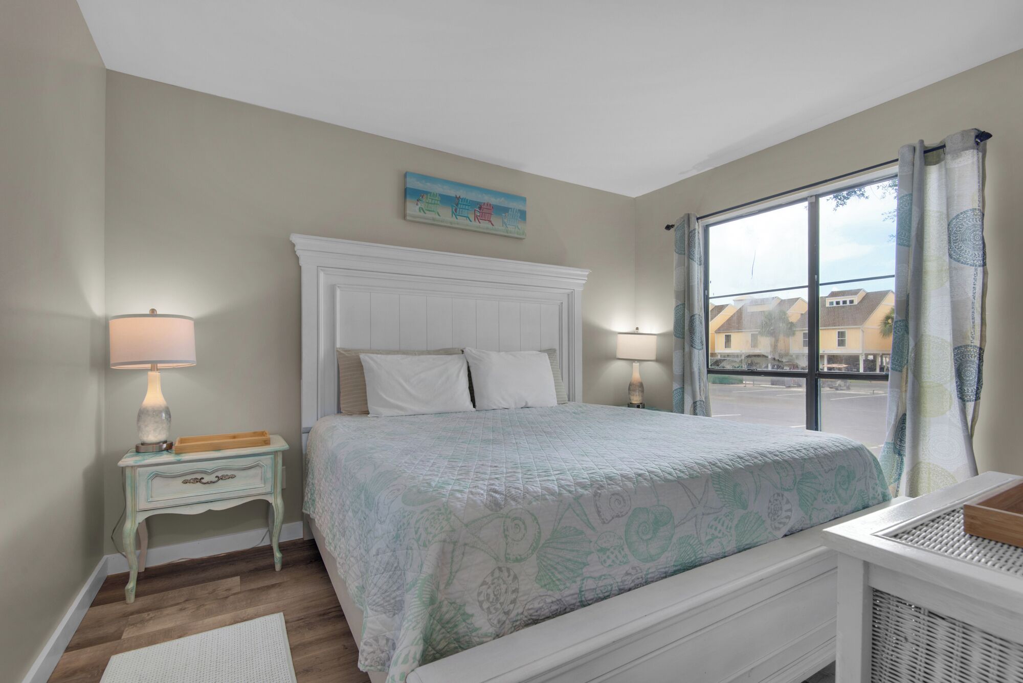 A bedroom with a bed, two bedside tables, a window with curtains, and a painting on the wall.