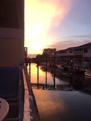 Ein Sonnenuntergangsblick vom Balkon mit Blick auf ruhiges Wasser und Gebäude im Hintergrund.