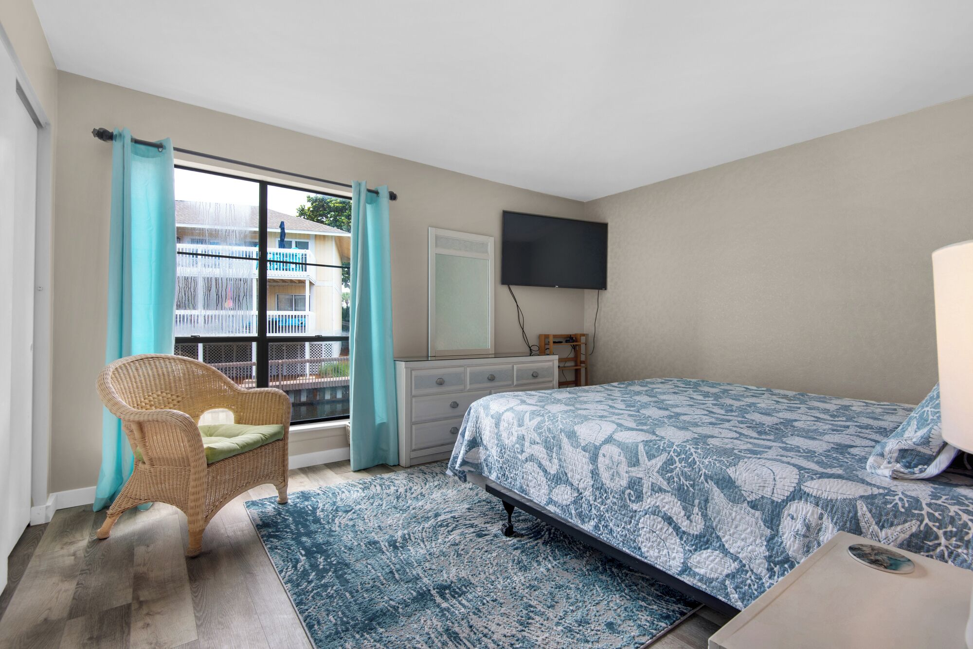 A bedroom with a bed, a dresser, a chair, a TV, and a window with curtains.