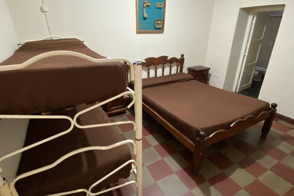 A room with a bunk bed, a small bedside table, a wall-mounted light, and a checkered floor.