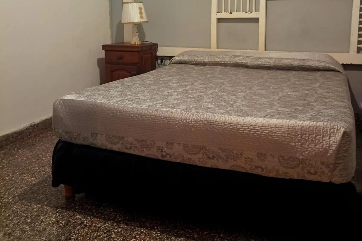 A bedroom with a bed, a nightstand, a lamp, and a wall decoration.
