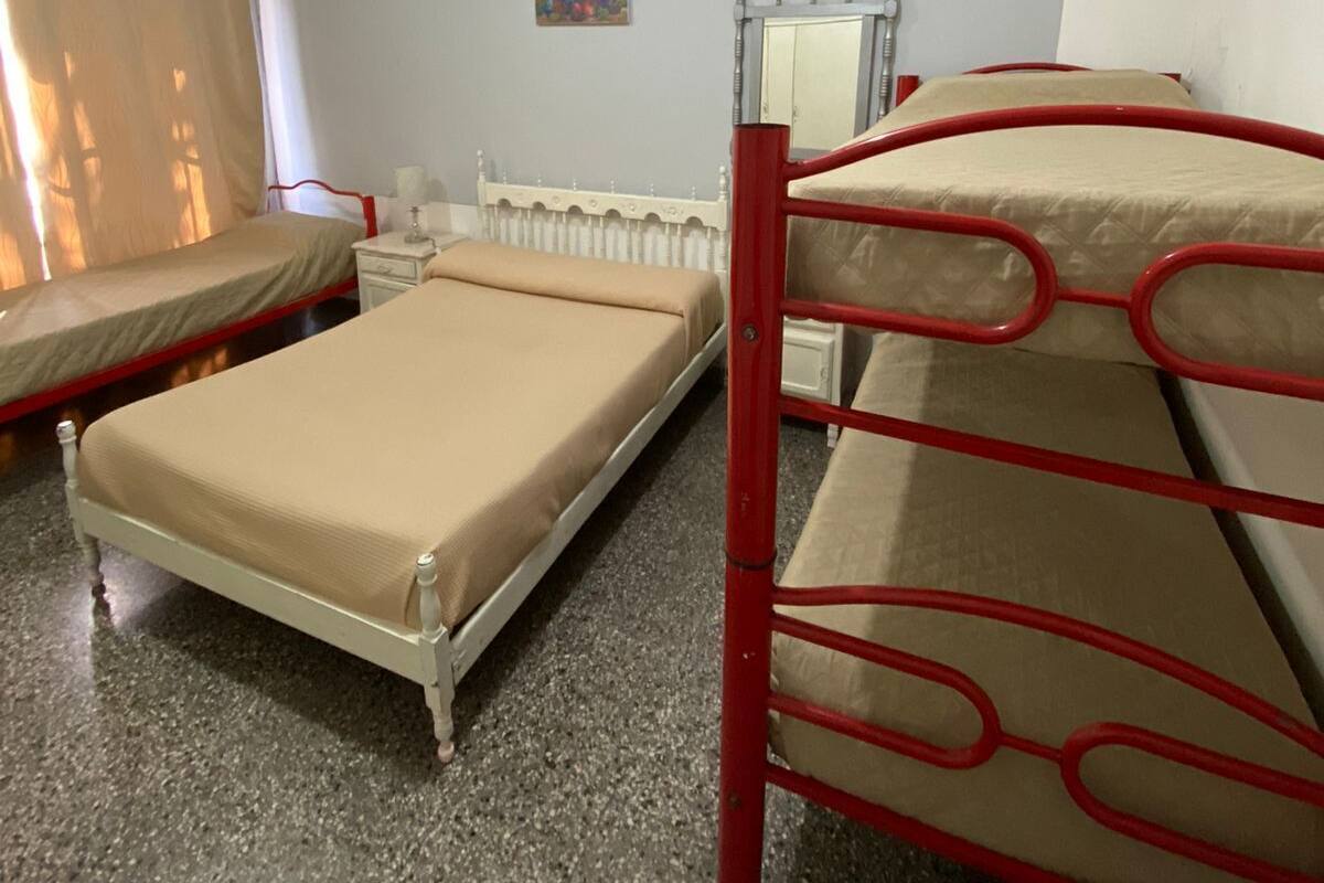 A dormitory room with bunk beds, a small bedside table, a mirror, and a radiator.