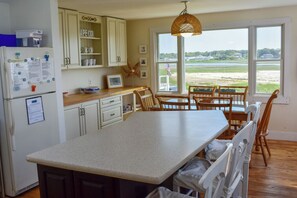 Une cuisine dotée d’un grand îlot central, de chaises en bois et offrant une vue sur la plage par la fenêtre.