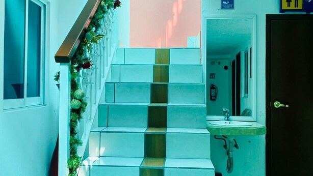 A staircase with a handrail, leading to a room with a sink and a door marked with a restroom symbol.