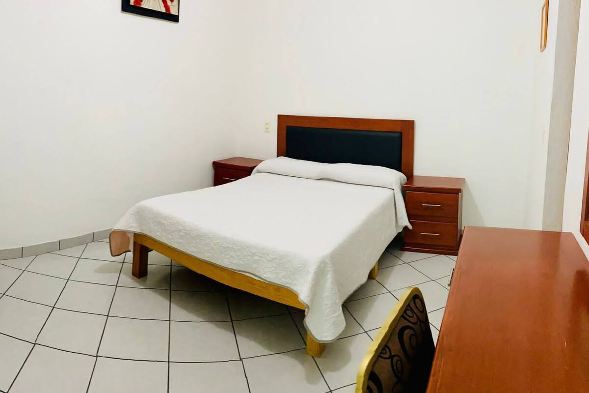 A neatly arranged bedroom with a bed, bedside tables, and a chair.