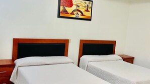 A hotel room with two single beds, wooden headboards, white bedding, a nightstand, and a framed painting on the wall.