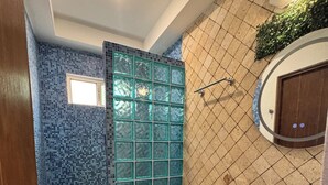 A bathroom with a glass sink, a toilet, and a shower area.