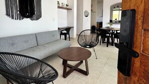 A modern living room with a grey sofa, black wireframe chairs, a wooden coffee table, and a ceiling fan.