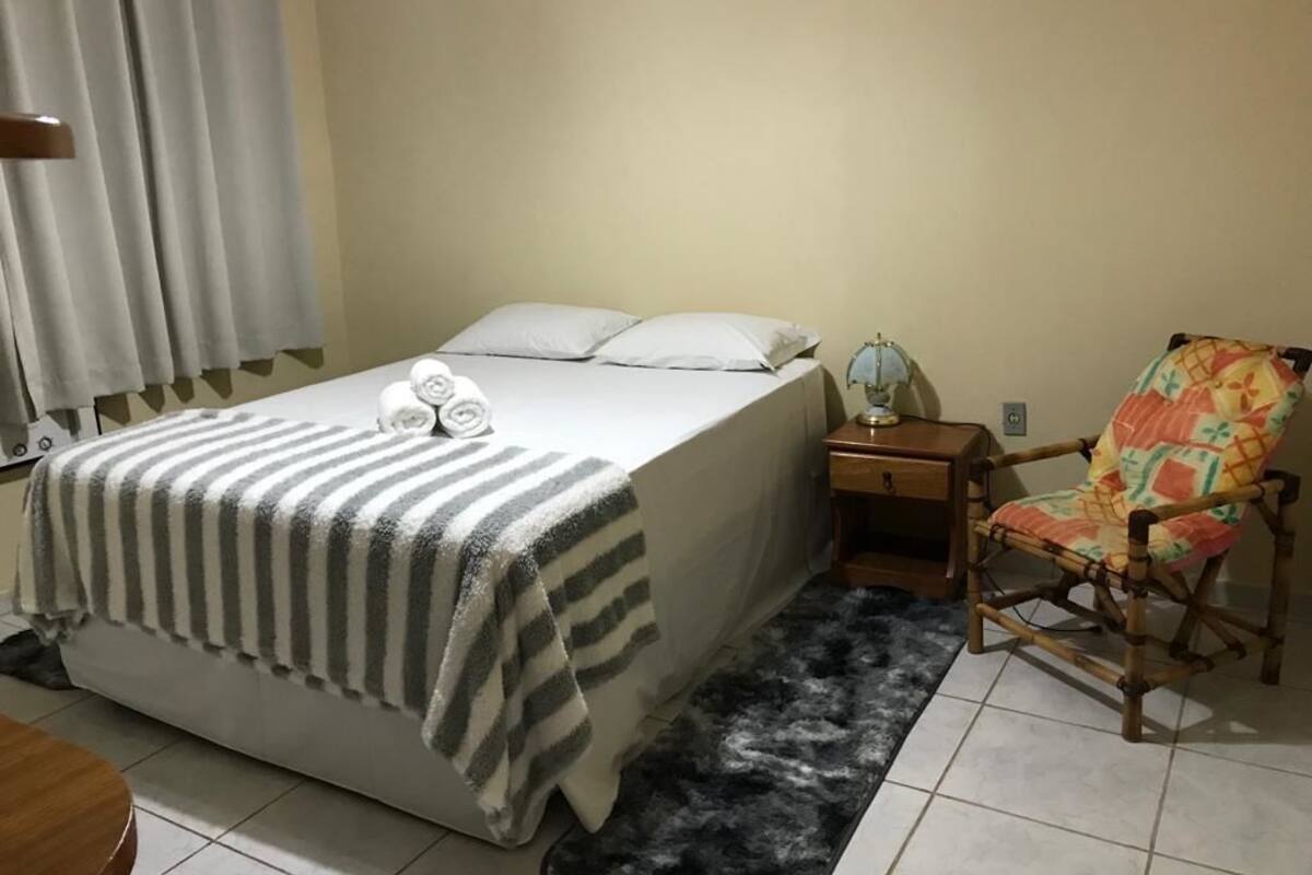 A bedroom with a bed, a chair, a nightstand, and a lamp.