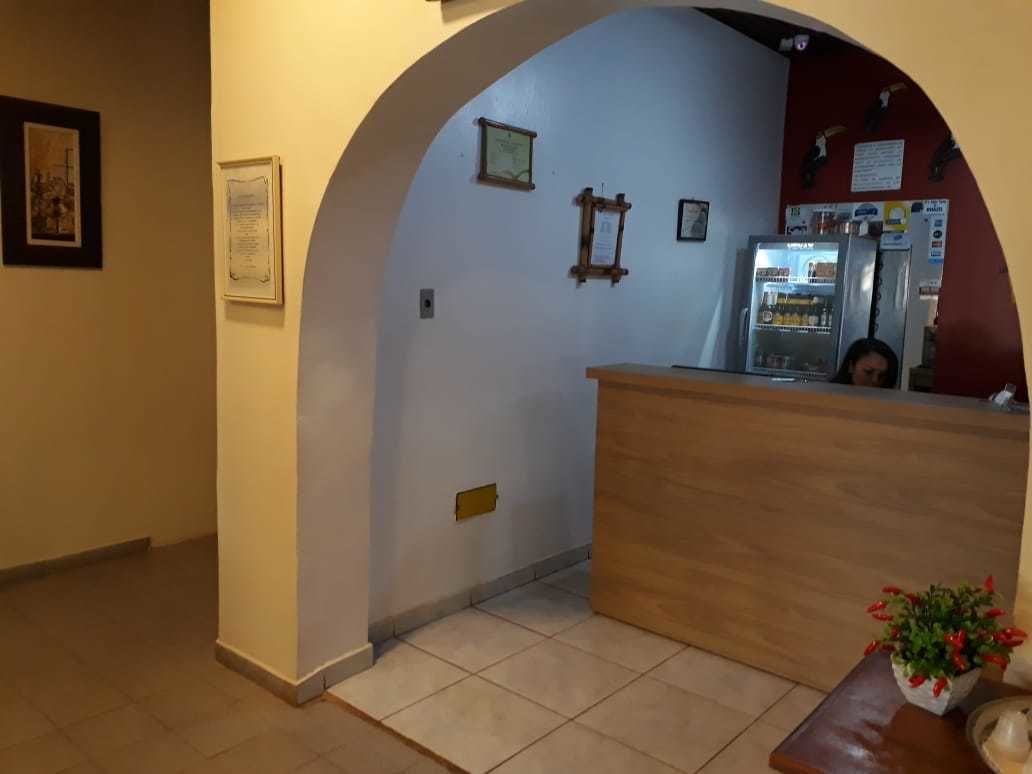 A reception area with a wooden counter, a person behind it, and a small table with a plant.