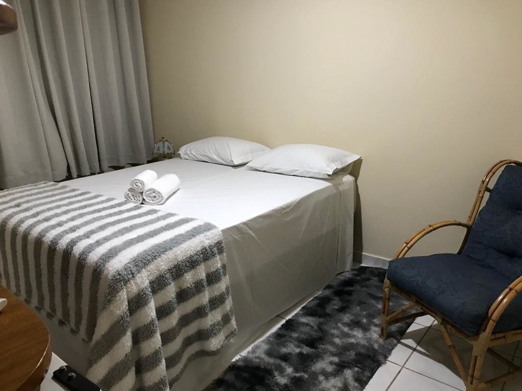 Una cama bien hecha con una colcha a rayas, una silla azul y un felpudo de pelo blanco y negro.