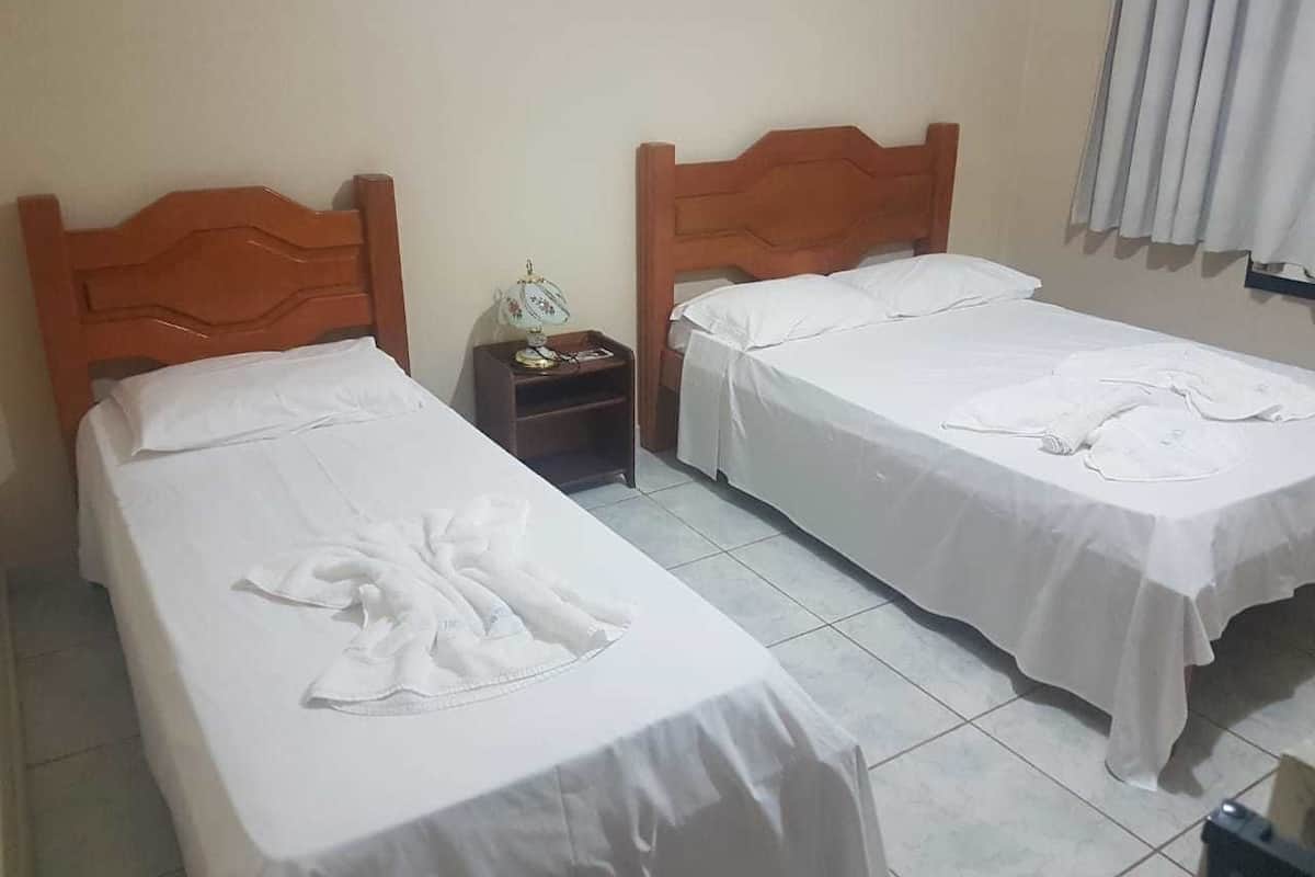 A hotel room with two single beds, a nightstand, and a small table with a lamp.