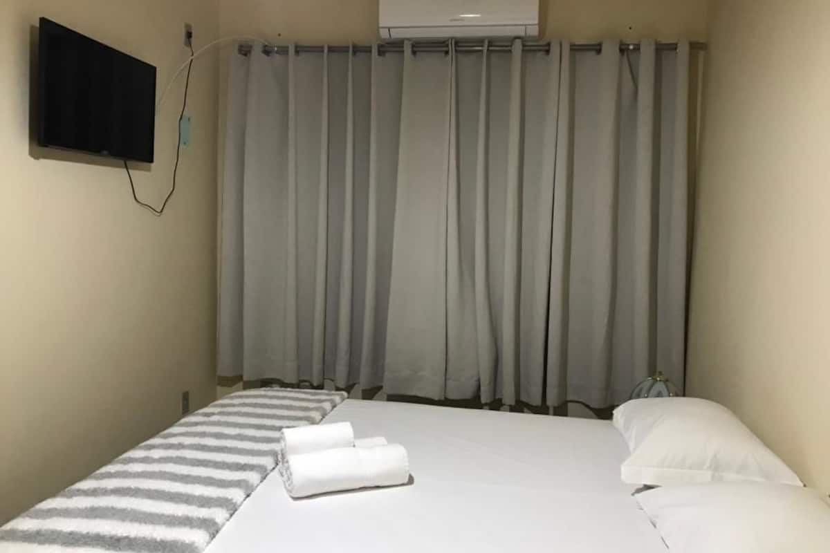 A hotel room with a bed, a TV mounted on the wall, and a window with curtains.