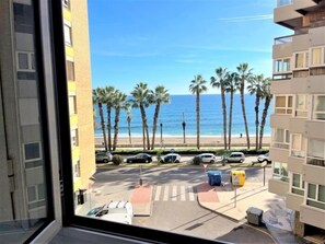 Vista desde una ventana con vista a una playa, palmeras, un estacionamiento y un edificio con balcones.