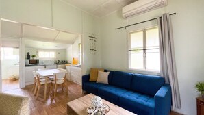 Un espacio habitable compacto con comedor, kitchenette y un sofá azul cerca de una ventana.