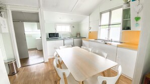 Cocina compacta con muebles blancos, microondas y estufa. Hay una mesa de comedor con sillas y una ventana sobre el fregadero.