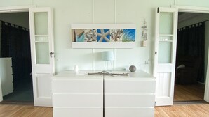 Una habitación con un tocador blanco, un cuadro encima y una lámpara sobre el tocador.