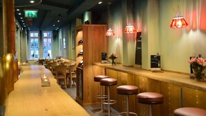 A restaurant with a long wooden counter, bar stools, hanging pendant lights, and a view of the street through large windows. - CENTRINUM Altstadt-Hotel (Melsungen)