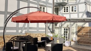 An outdoor seating area with a red umbrella, wicker furniture, and a stone wall. - CENTRINUM Altstadt-Hotel (Melsungen)