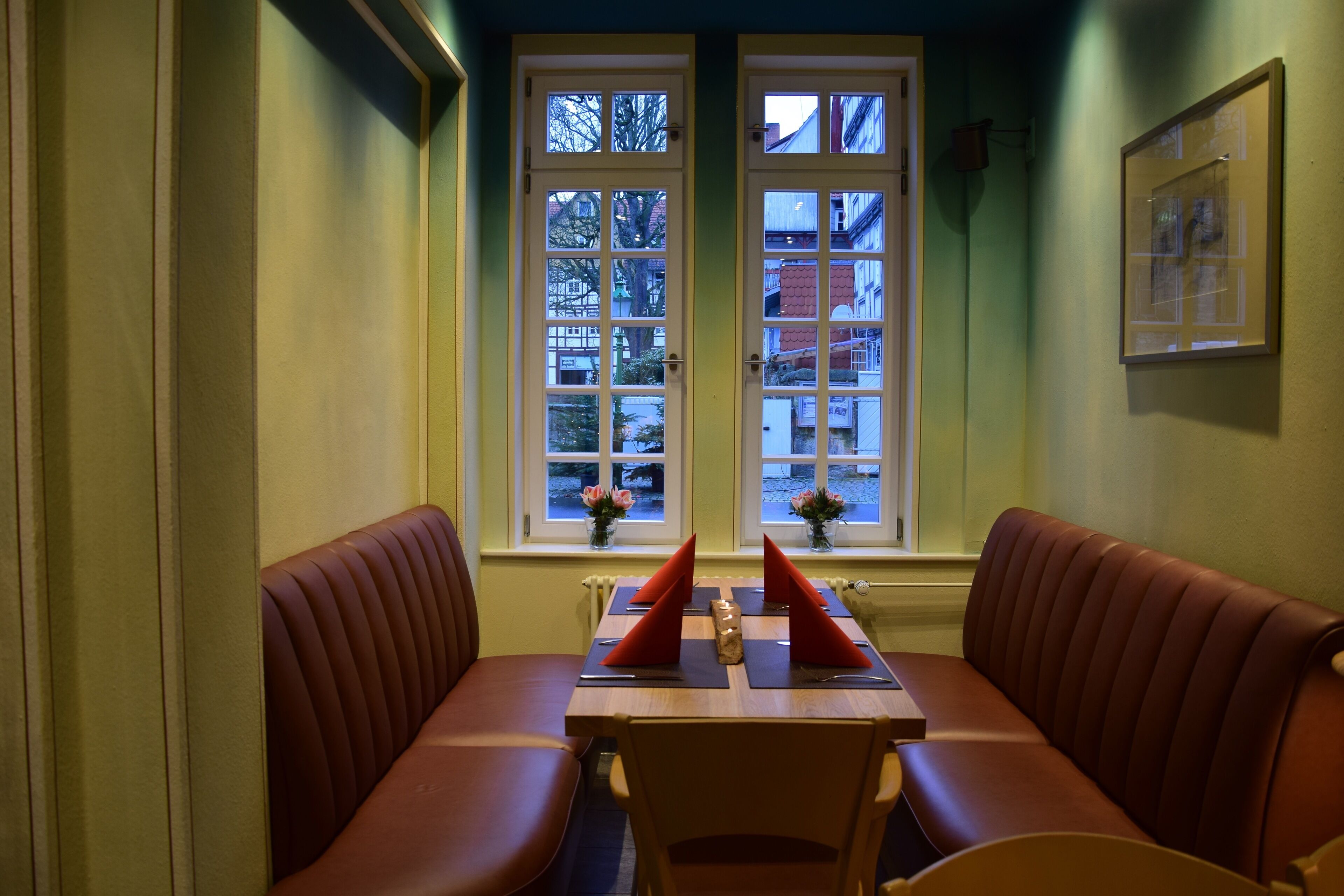 Ein Restaurant mit einer U-förmigen Sitzbank, einem Tisch mit roten Servietten und Fenstern mit Blick nach draußen.